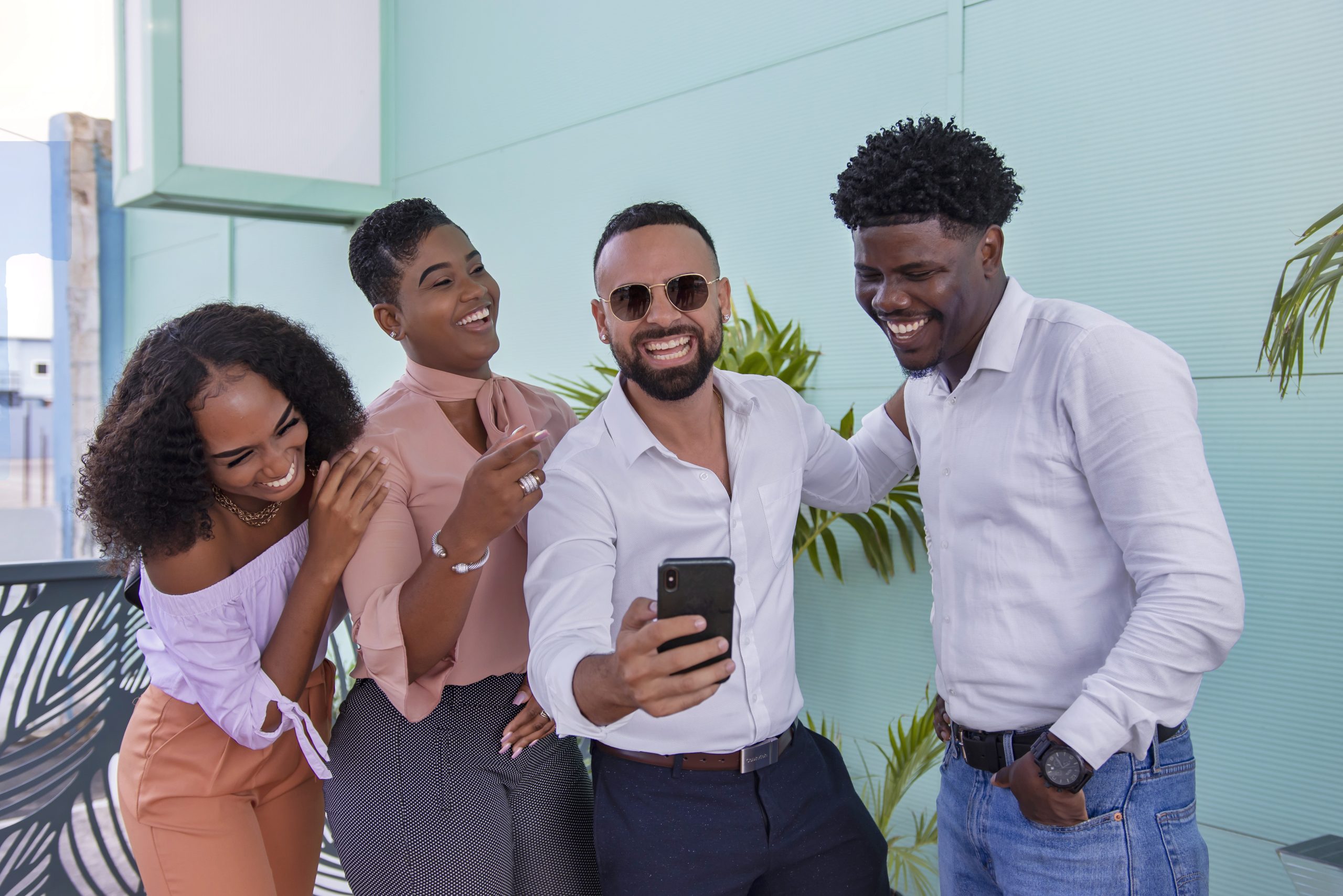 Man showing something on his phone to another man and two woman. They are all laughing.