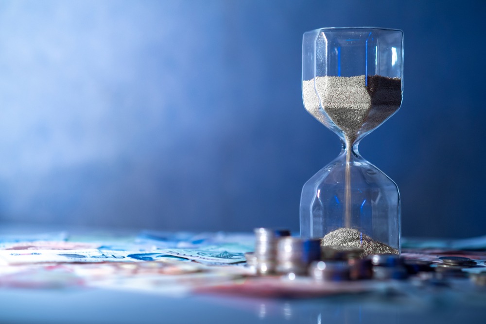 Sand running through an hourglass on a table with money.